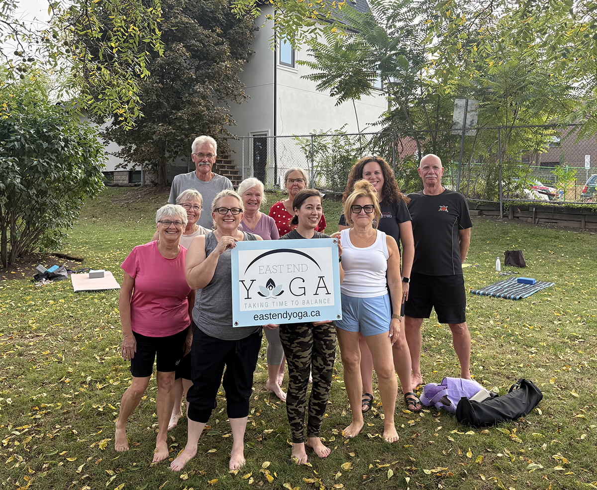 East End Yoga group outdoors holding the East End Yoga sign